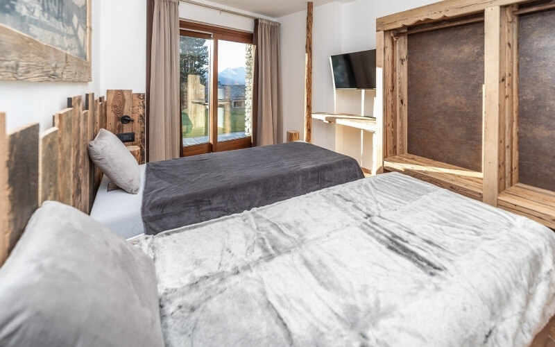 Cozy room with two angled beds, a desk with a TV, and a window showing trees and mountains outside.