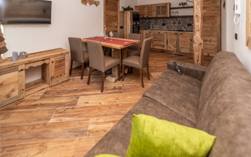 Cozy living and dining area with wood tones, a brown couch, dining table, and a glimpse of a kitchen in the background.