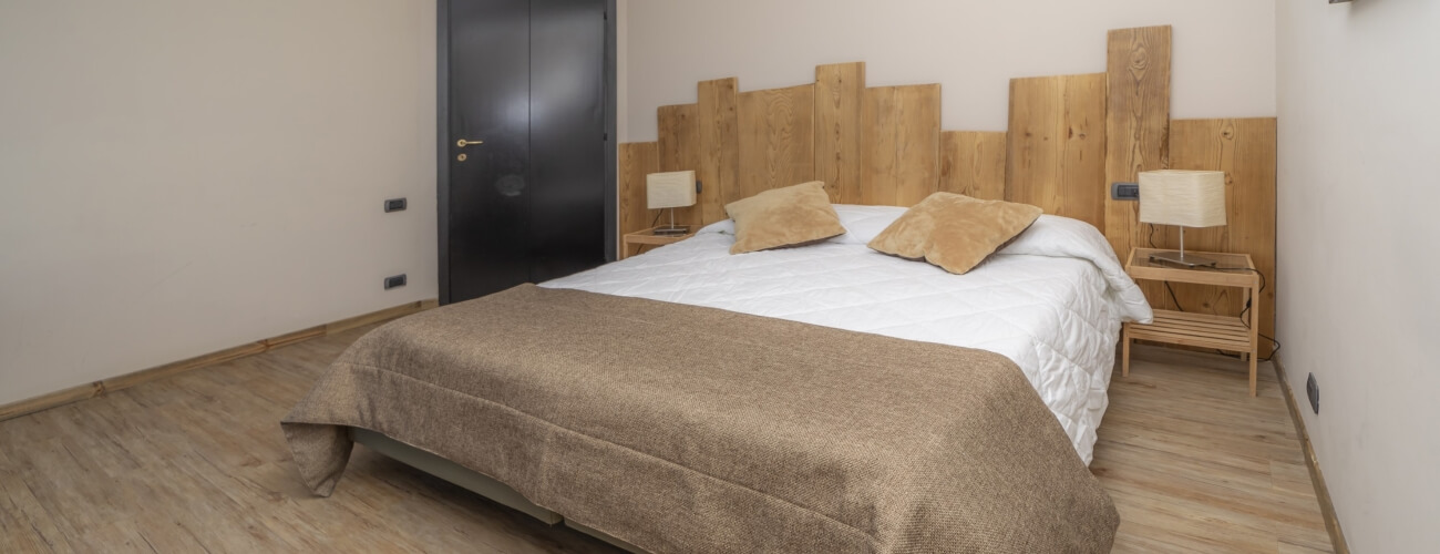 Serene bedroom with a white bed, light-brown pillows, wooden headboard, nightstands, and calming ambiance.