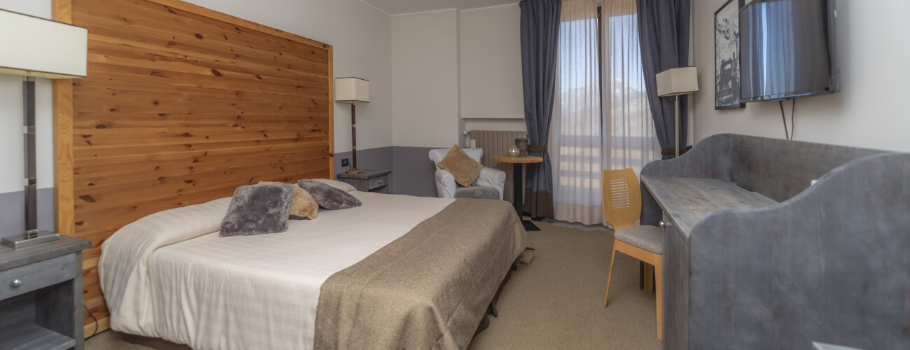 Serene hotel room with neutral colors, wooden accents, a bed with pillows, nightstands, a chair, and a window with curtains.