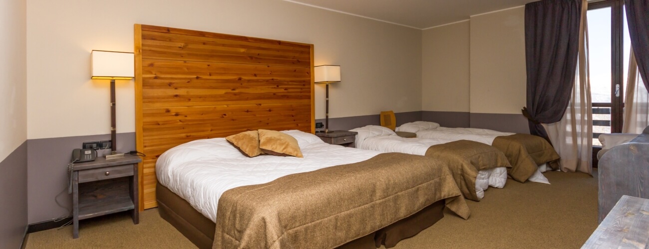 Hotel room with two beds, beige and brown decor, wooden headboard, nightstands, large window, and light brown carpet.