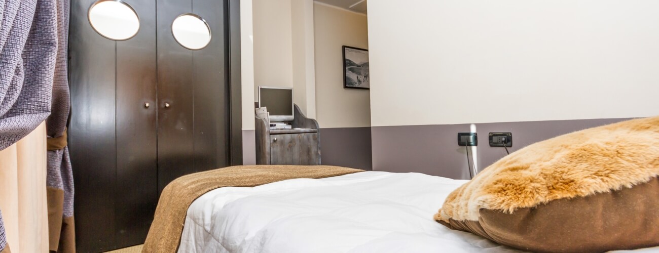 Hotel room featuring a bed with white comforter, closet, computer desk, and dark brown double doors with round windows.