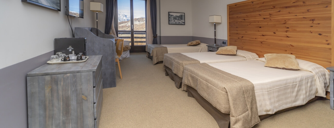 Camera d'albergo con due letti, un dresser, TV e vista sulle montagne attraverso una grande finestra.