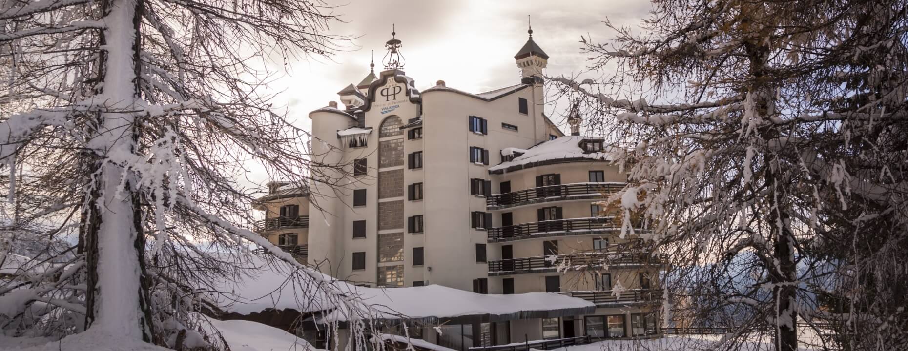 Large multi-story building with snowy exterior, "HP" sign, surrounded by snow-covered trees under an overcast sky.