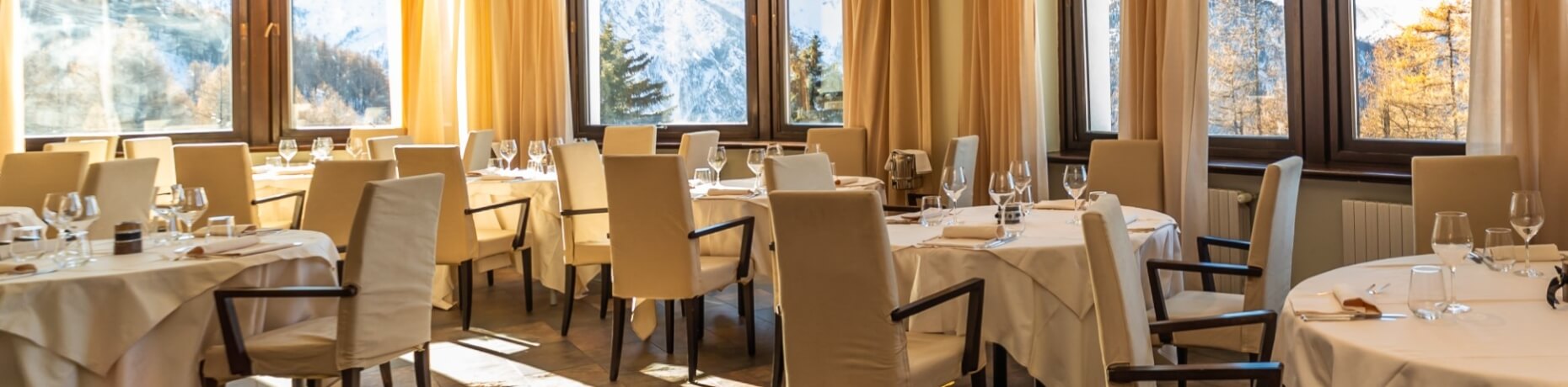 Elegant dining room with round tables set for a formal meal, large windows offering a scenic mountainous view.