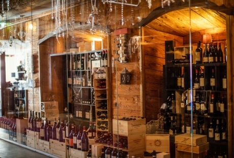 A cozy wine shop with a glass storefront, wooden walls, and shelves displaying various wine bottles and decorative elements.