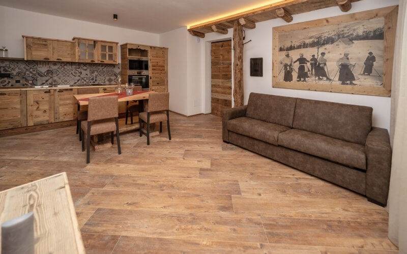 Cozy living room with kitchen, brown couch, dining table, and black-and-white skiing photo on the wall.