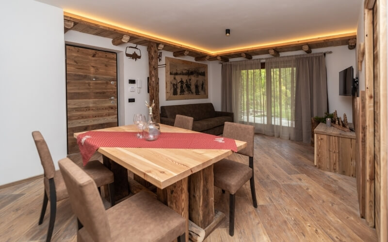 Open-concept living space with a wooden dining table, dark couch, large windows, and rustic-modern decor for a cozy ambiance.