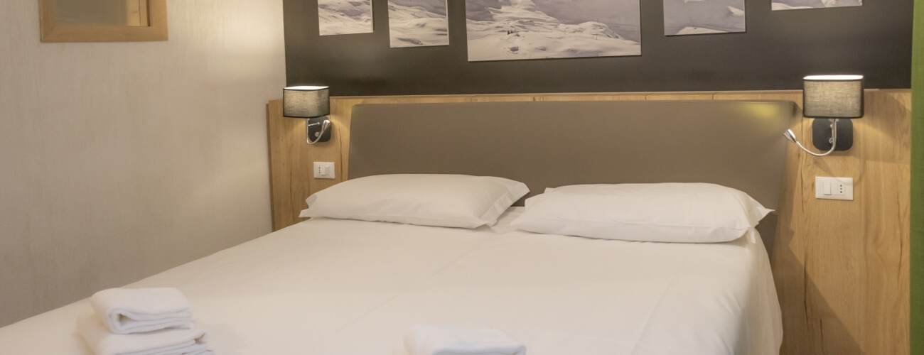 Camera da letto serena con letto bianco, fotografie in bianco e nero, lampade grigie e asciugamani piegati.