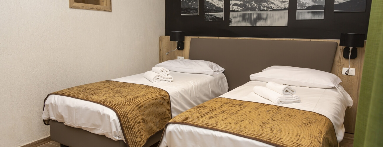 Hotel room with two beds, brown headboard, black-and-white photos, sconces, nightstand, and green curtain.