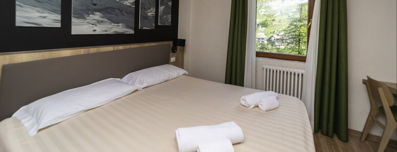 Camera da letto serena con letto grande, comforter chiaro, fotografie in bianco e nero e vista su alberi e colline.