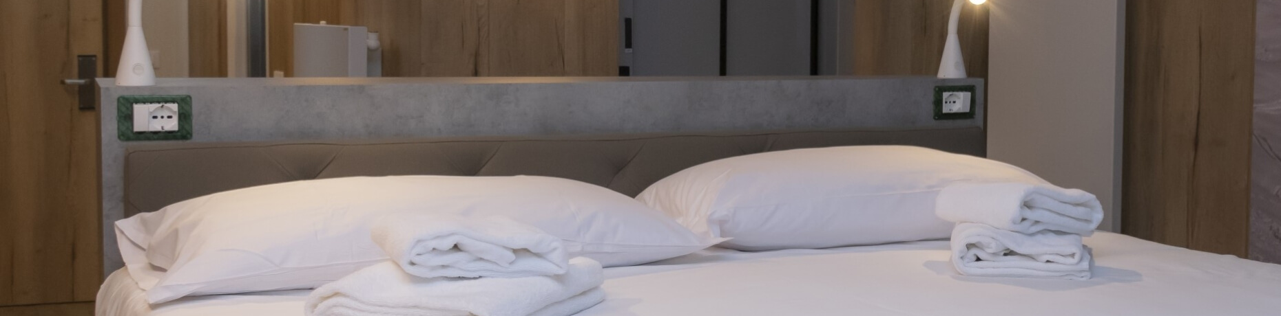 Hotel room featuring a neatly made bed, nightstands with lamps, towels, and a wall-mounted mirror with a vase.