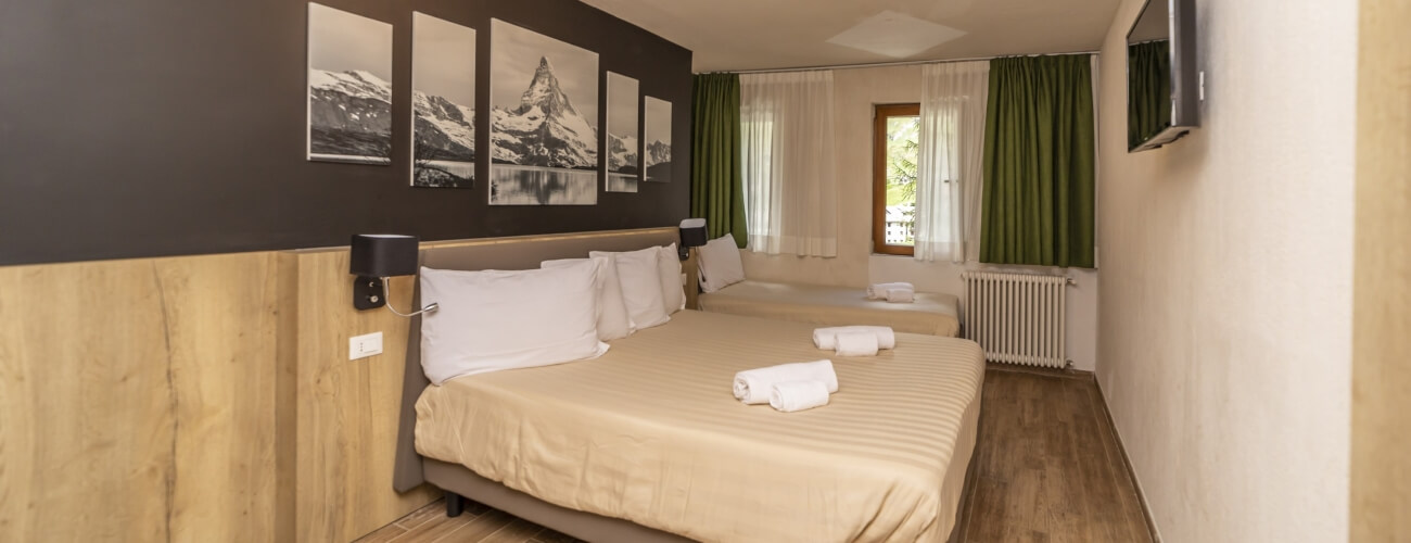 Hotel room with two beds, mountain photographs, window with green curtains, and a flat-screen TV on a hardwood floor.