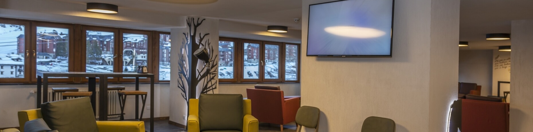 Cozy lounge with yellow and orange chairs, large window view of snowy landscape, and whimsical branch-like light fixture.