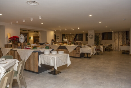 Spacious buffet room with white tablecloths, well-lit, featuring tables of dishes, chairs, and a window with curtains.