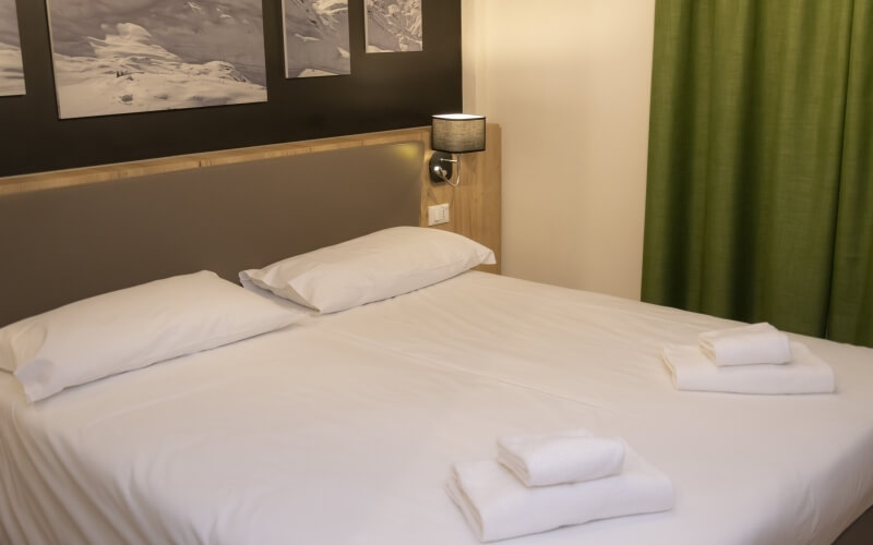 Serene bedroom with a neatly made bed, white linens, wall art, soft lighting, and natural light from an open window.