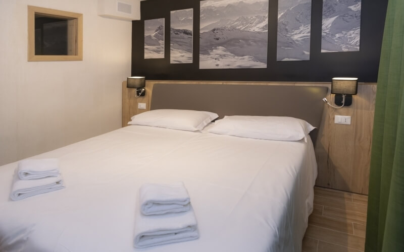 Cozy hotel room with a large bed, white linens, landscape paintings, and dark green curtains, featuring USB-equipped sconces.