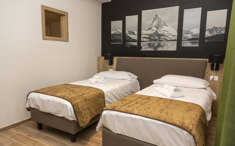 Hotel room with two twin beds, black wall with mountain pictures, light tile floor, and a green curtain. Clean and simple decor.