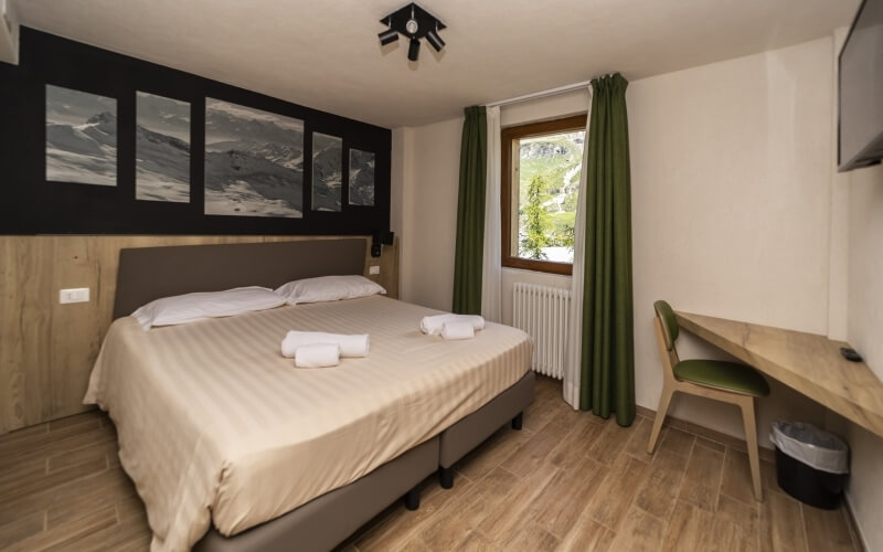 Serene bedroom featuring a queen bed with tan comforter, black-and-white photos, green curtains, and a wooden desk.