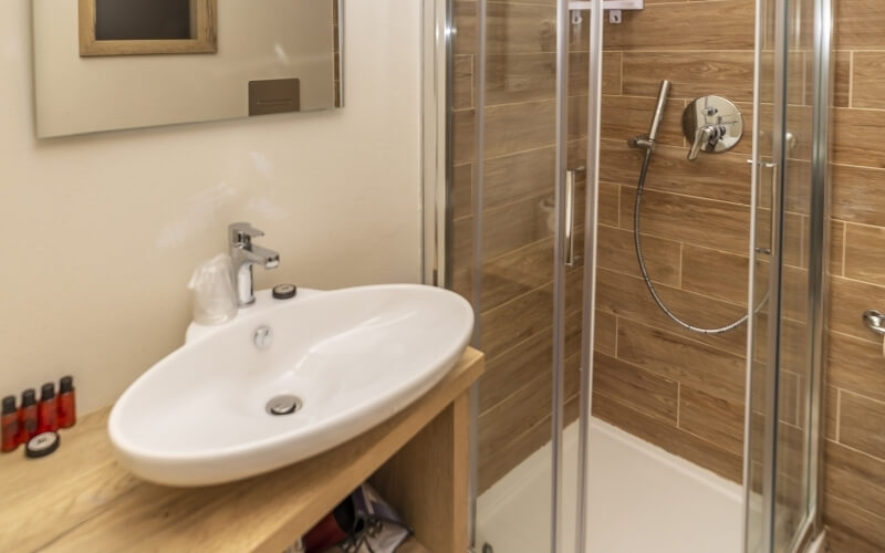 Bathroom featuring a glass-enclosed shower, white sink, mirror, wooden counter with bottles, and beige walls.