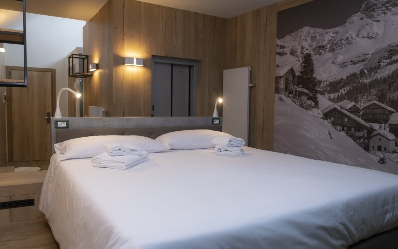 Serene hotel room with a spacious bed, warm lighting, modern decor, and a striking mountain photograph on the wall.