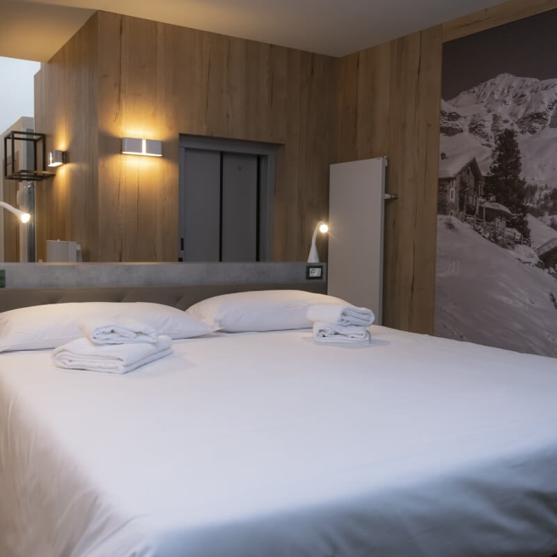 Hotel room with a large bed, wooden walls, mountain mural, and warm lighting, creating a serene and inviting atmosphere.