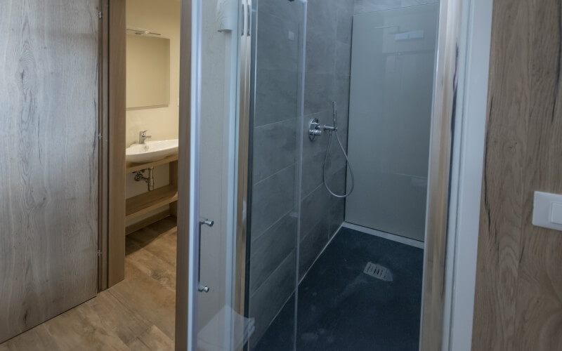 Modern bathroom featuring a shower with glass door, sink with white countertop, and light wood flooring.