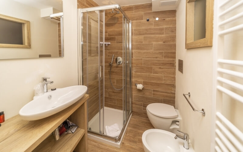 Modern bathroom featuring a glass-enclosed shower, white toilet, oval sink, and brown tiled walls and floor.