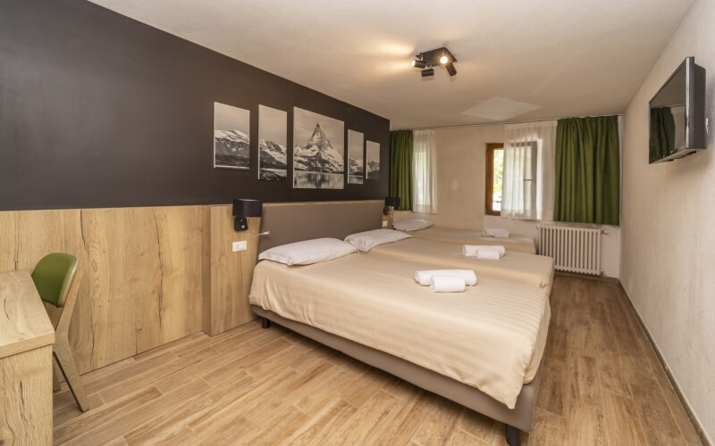 Cozy hotel room with two beds, a desk, and a green chair, featuring mountain pictures on dark gray walls.