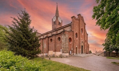 A brick church with a clock tower, surrounded by trees and grass, under a pink and orange sky at sunset or sunrise.