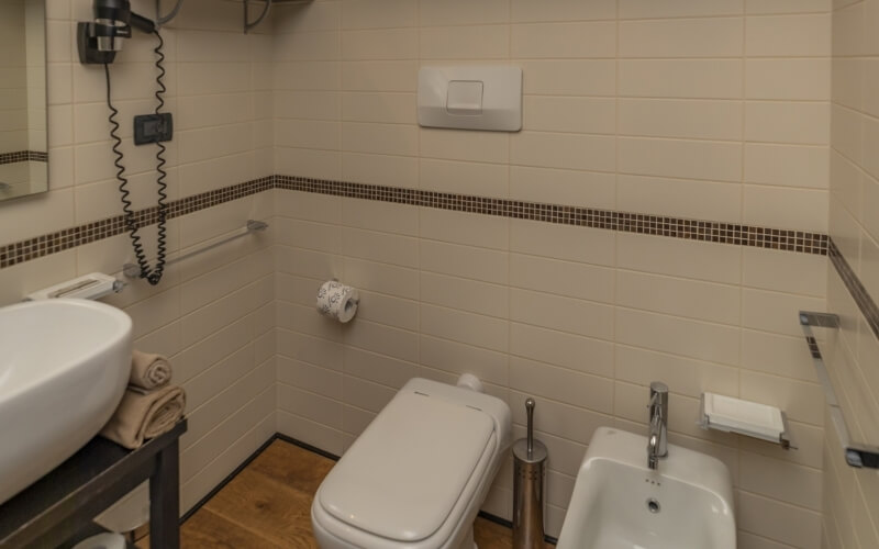 A clean bathroom with beige tiled walls, wooden floor, white toilet, sink, bidet, and modern fixtures.