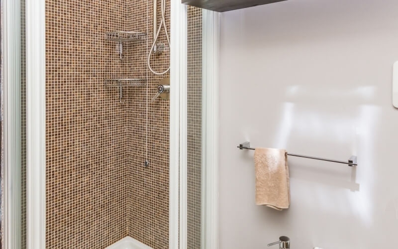 Bathroom with a shower featuring brown tiles, a towel rack with a light-brown towel, and a silver faucet below.