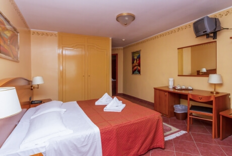 Camera d'albergo accogliente con letto, scrivania, specchio, TV e armadio, decorata con opere d'arte e luce calda.