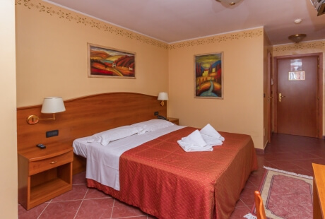 Cozy hotel room with a double bed, red coverlet, abstract art, warm peach walls, and a ceiling fan.