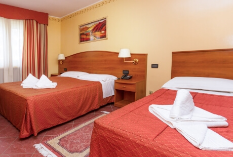 Camera d'hotel vivace con letti, coperte rosse, asciugamani a forma di cigno e finestre con tende a righe verticali.