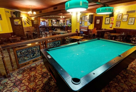 Una scena vivace di un pub con un tavolo da biliardo, bar illuminato e atmosfera accogliente.