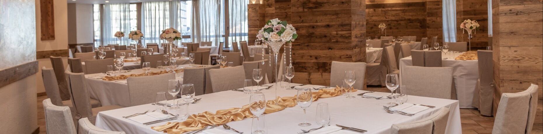 Elegant wedding reception hall with long tables, white tablecloths, gold runners, and floral centerpieces.