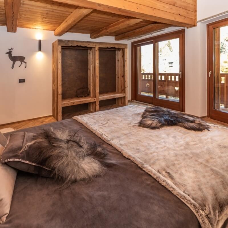 Cozy rustic bedroom with a plush bed, wooden accents, soft lighting, and French doors revealing a tranquil outdoor view.