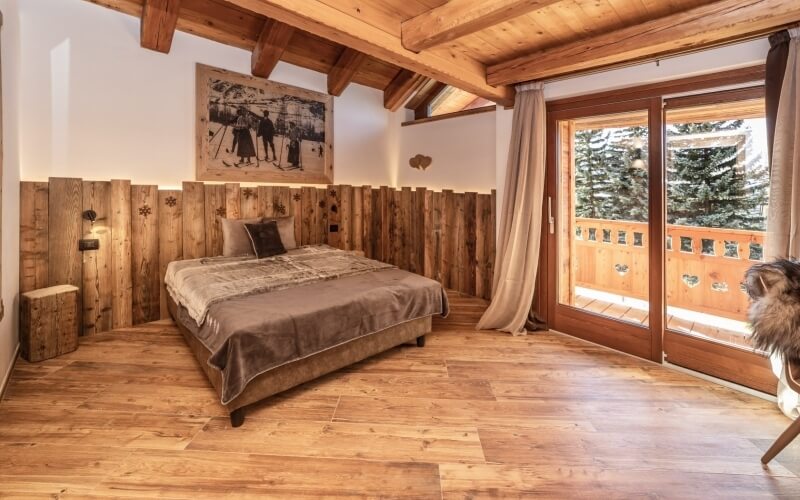 Camera accogliente con letto, finestre panoramiche, pareti in legno e arte invernale, che trasmette calore e serenità.