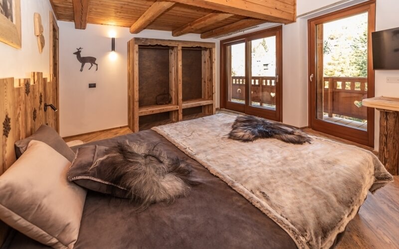 Cozy bedroom with a large bed, wooden cabinet, deer wall art, sliding doors to a balcony, and a flat-screen TV.