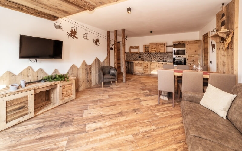 Soggiorno e cucina rustica con mobili in legno, TV a parete e decorazioni accoglienti, ideale per relax e socializzazione.