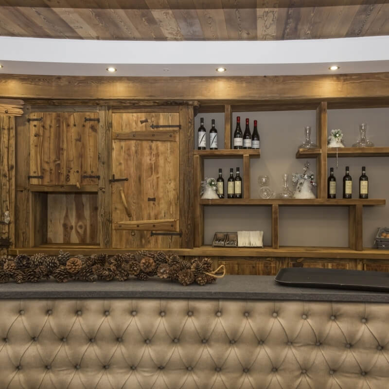 Stylish wooden bar with leather upholstery, rustic pinecone centerpiece, and textured shelves displaying glassware in a cozy setting.