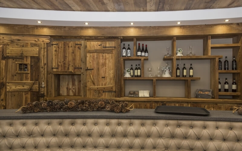 Rustic bar with wooden accents, tufted leather countertop, pinecones, and wine bottles on wooden shelves, creating a cozy atmosphere.