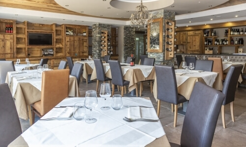 Elegant dining area with fine linens, glassware, leather chairs, wine shelves, and a chandelier, ideal for upscale events.