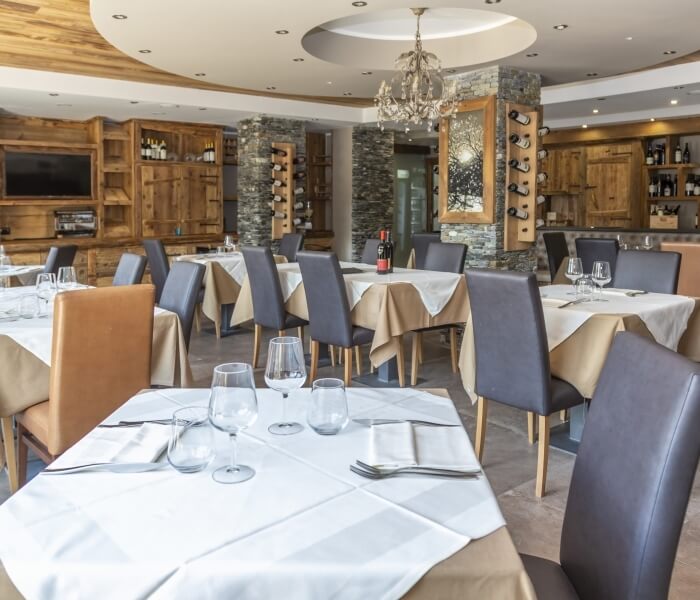 Modern restaurant dining area with set tables, a bar, chandelier, and stylish decor.