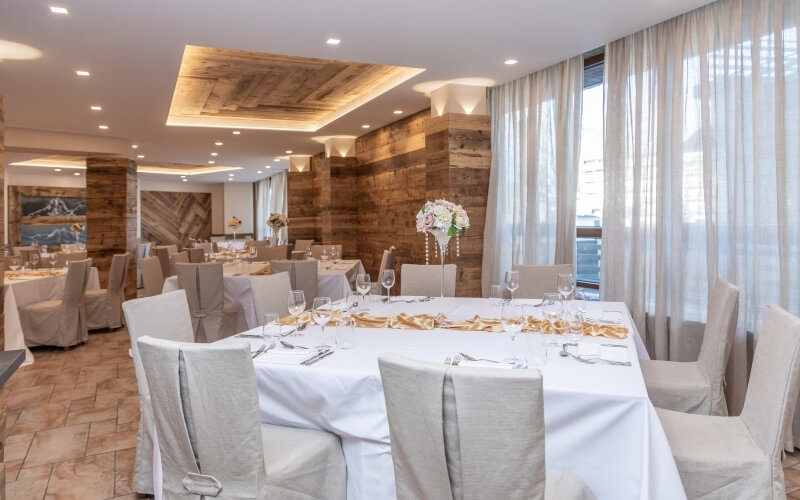 Elegant dining room with white decor, brown accents, tables set for formal events, and a mountain painting in the background.