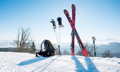 Serene winter scene with skis, poles, and a backpack in snow, against a blue sky and mountain range in the background.