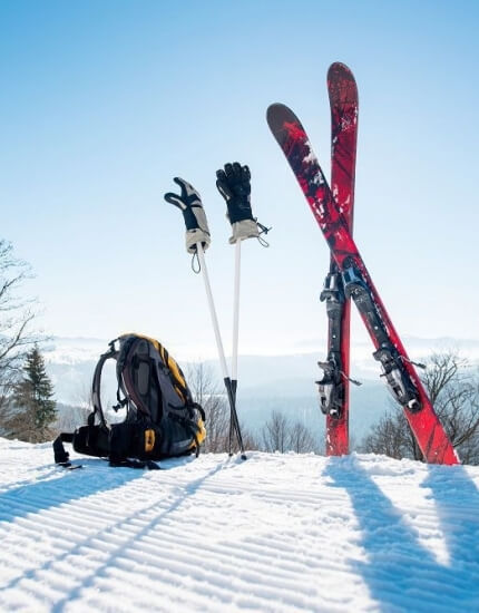 Snowy landscape with red skis, a black backpack, and ski poles in the foreground, set against a serene mountain backdrop.