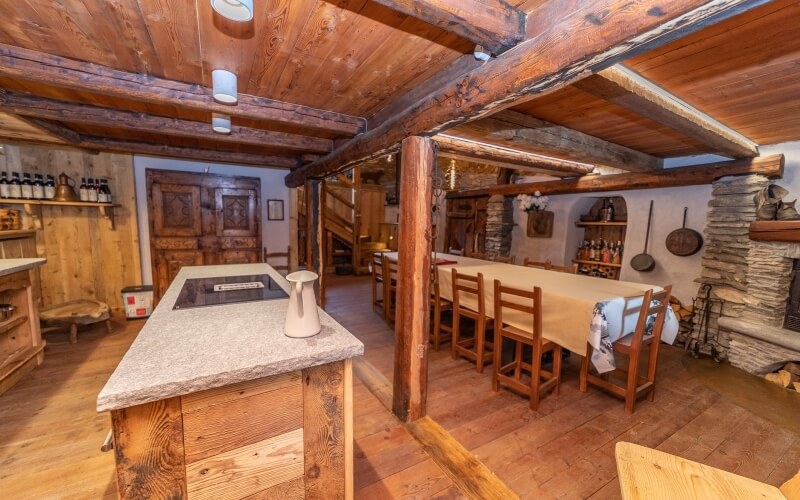 Rustic kitchen with wooden beams, central island, stone fireplace, and dining area, creating a warm, inviting atmosphere.