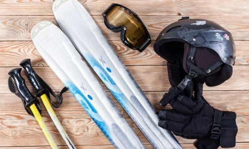 Winter sports equipment arranged on wooden surface: skis, helmet, gloves, goggles, and ski poles.